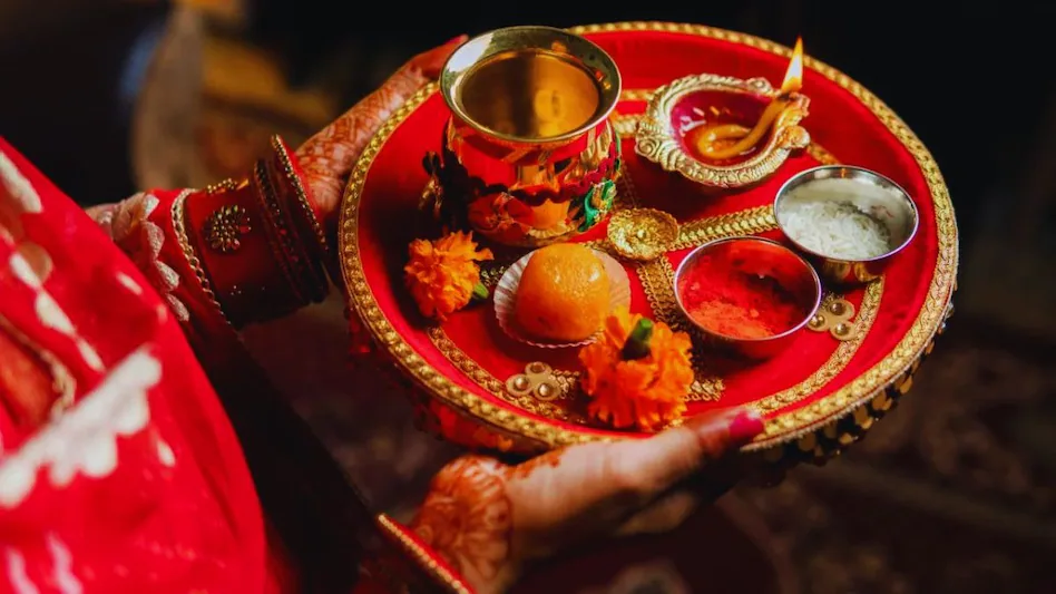 करवा चौथ की पूजा थाली, जिसमें दीपक, जल का कलश, रोली और चावल रखे हैं, एक महिला लाल साड़ी पहने हुए है।