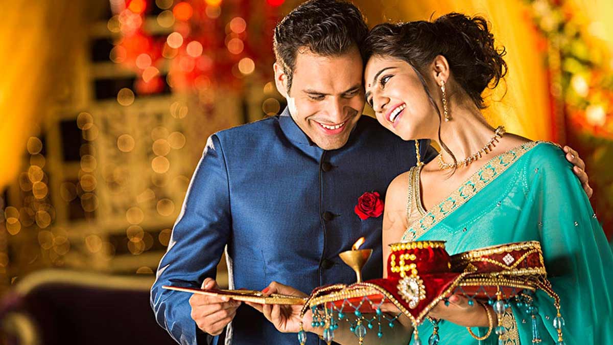 एक कपल करवाचौथ मना रहा है, जहाँ पत्नी पूजा की थाली लिए है और पति उसके साथ खड़ा है, यह इस त्योहार के महत्व और गिफ्ट देने के अवसर को दर्शाता है।