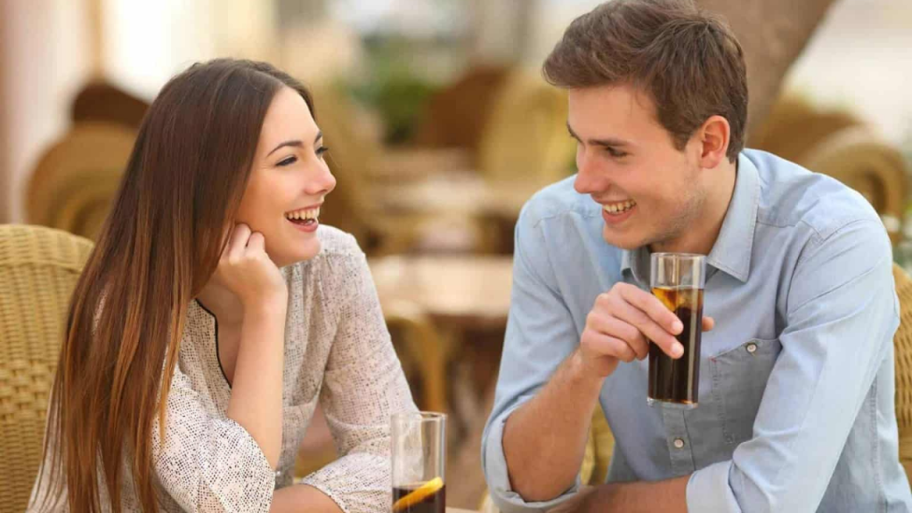 एक कैफे में कॉफ़ी पीते हुए हँसते हुए कपल, जो दर्शाता है कि खुशहाल बातचीत भी True Love Signs में से एक है।