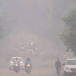 दिल्ली में बढ़ते प्रदूषण के कारण धुंध से ढकी सड़कों और मास्क पहने लोगों का दृश्य।