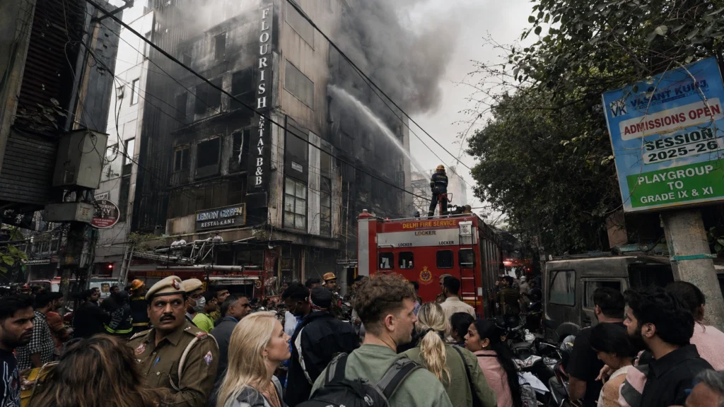 Thick smoke billowing from the top floors of the Flourish Stay B&B building during the tragic Malviya Nagar hotel fire in Delhi as fire services operate in a congested market lane.