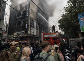Thick smoke billowing from the top floors of the Flourish Stay B&B building during the tragic Malviya Nagar hotel fire in Delhi as fire services operate in a congested market lane.