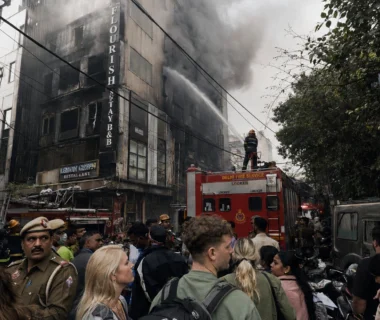 Thick smoke billowing from the top floors of the Flourish Stay B&B building during the tragic Malviya Nagar hotel fire in Delhi as fire services operate in a congested market lane.